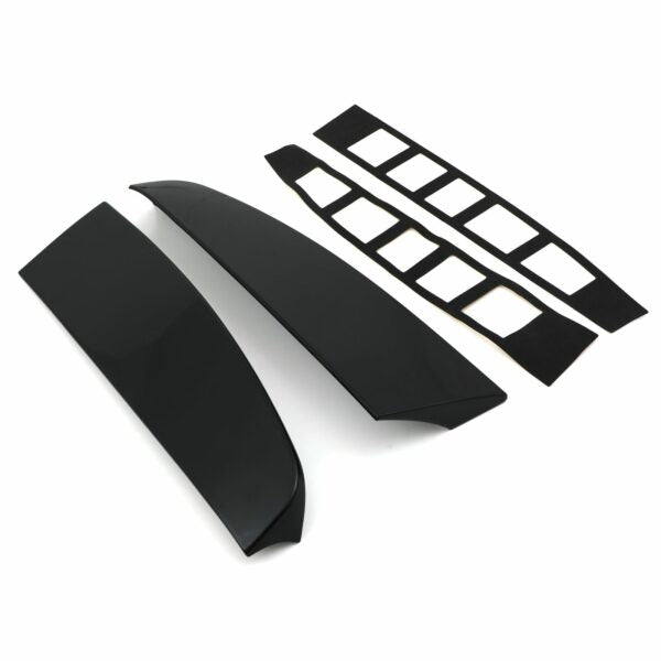 Two glossy black car spoiler pieces lay parallel, accompanied by two sets of adhesive strips with rectangular cutouts, all set against a plain white background.