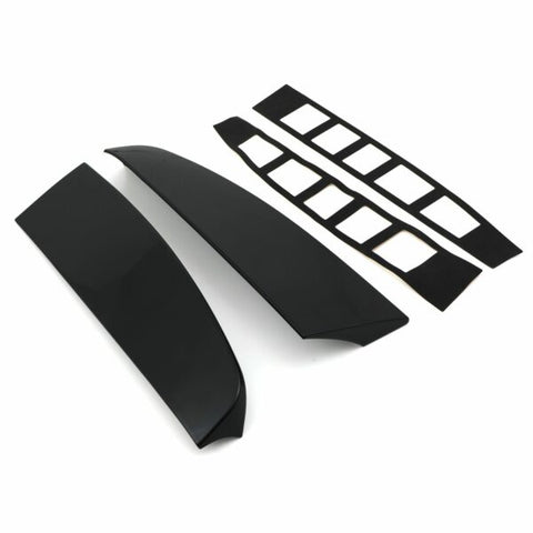Two glossy black car spoiler pieces lay parallel, accompanied by two sets of adhesive strips with rectangular cutouts, all set against a plain white background.