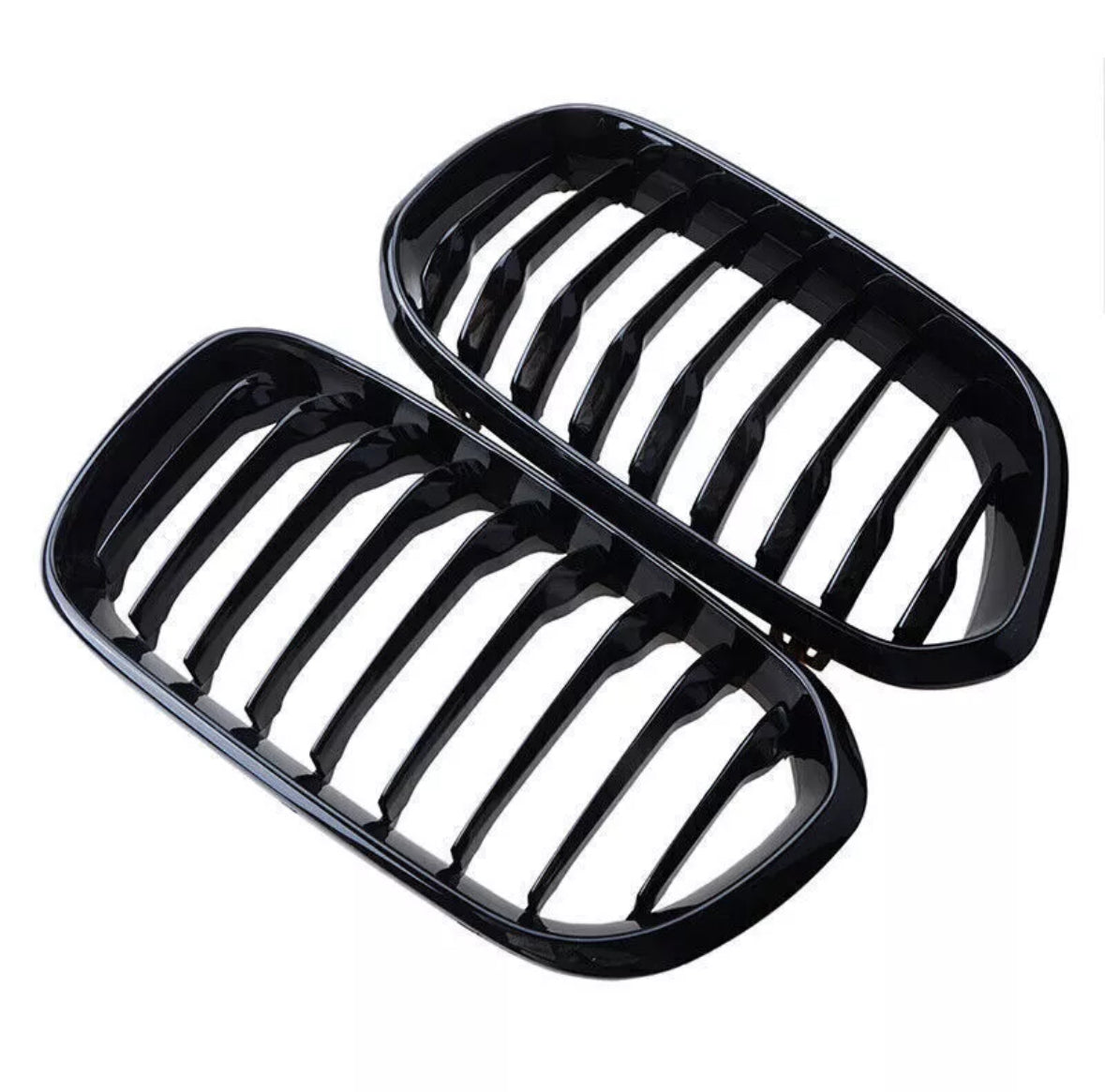 Two glossy black car grilles, each with multiple vertical slats, placed adjacent to each other against a white background.