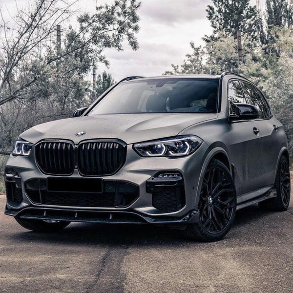 A matte grey SUV with a prominent grille sits parked on a paved road; surrounding trees create a serene, outdoor atmosphere.
