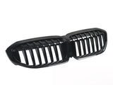 A shiny black car grille features dual kidney-shaped openings with vertical slats, presented against a plain white background.