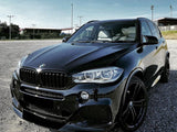 A sleek black BMW SUV is parked on a gravel lot. It sits under a clear blue sky, near empty sports fields with pole lights.