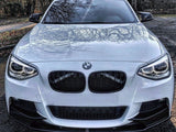 A white BMW car is parked on asphalt, with sunlight reflecting on the hood. Bare trees and foliage surround the area, casting shadows on the vehicle.