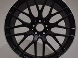 A black AMG car wheel rim with a multi-spoke design is displayed against a plain background, positioned upright on a circular white platform.