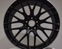 A black AMG car wheel rim with a multi-spoke design is displayed against a plain background, positioned upright on a circular white platform.
