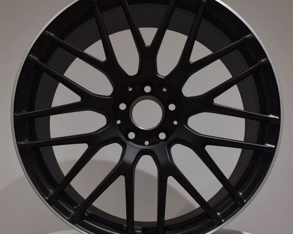 A black car wheel with multiple spokes displays the "AMG" logo at the top, set against a plain gray background on a white surface.