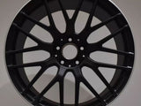 A black, multi-spoke AMG car rim is displayed upright against a neutral background, resting on a white surface.
