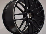 A black alloy wheel with a multi-spoke design resting on a white surface. It features an 