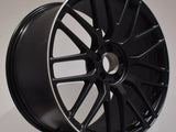 A black alloy wheel with a multi-spoke design rests vertically on display. The logo 