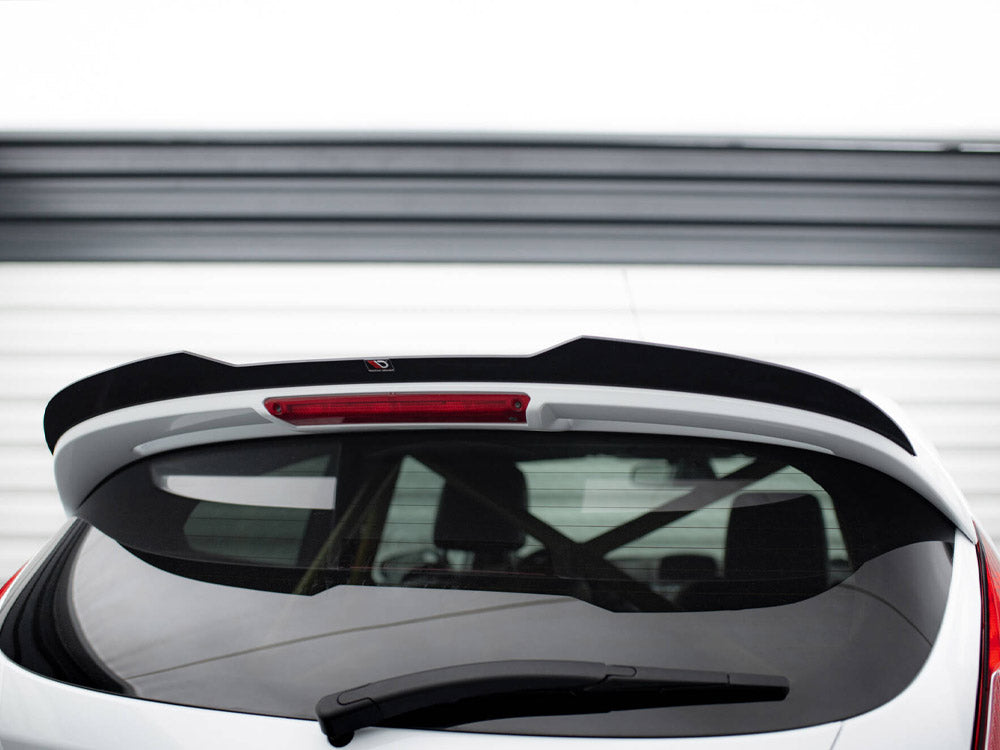 A white car's rear with a black spoiler and rear window wiper is pictured against a garage door. The spoiler has a small logo near the middle top.