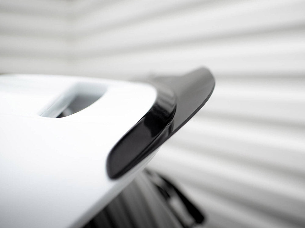 A sleek black and white car spoiler is attached to a vehicle, shown close-up. It's positioned in a brightly lit area with blurred, light-colored background lines.