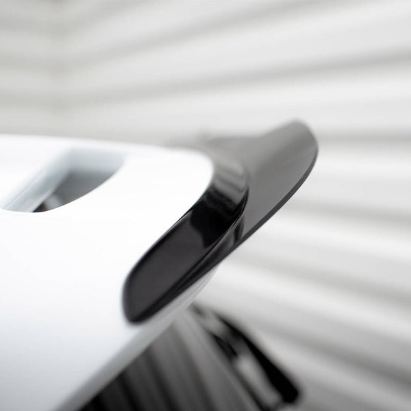 A sleek black and white car spoiler is attached to a vehicle, shown close-up. It's positioned in a brightly lit area with blurred, light-colored background lines.