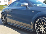 A dark blue sports car parked on a sunlit driveway, featuring large black alloy wheels with silver spokes and a 