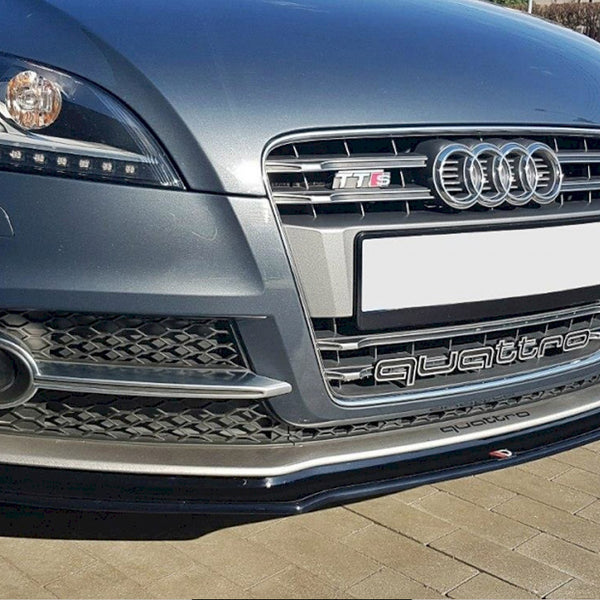 The image shows the front bumper of an Audi car with "TTS" and "quattro" logos. The vehicle is parked on a paved surface with a clear sky above.