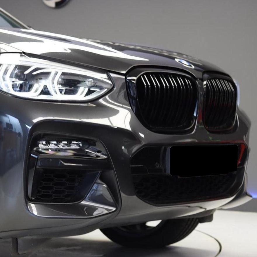 A sleek, gray car exhibits an illuminated headlight and prominent grille; it is positioned indoors, suggesting a showroom environment. No text is present.