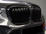 The car's front features a glossy black grille with vertical slats, displaying the BMW emblem on the hood, set against a blurred indoor background.