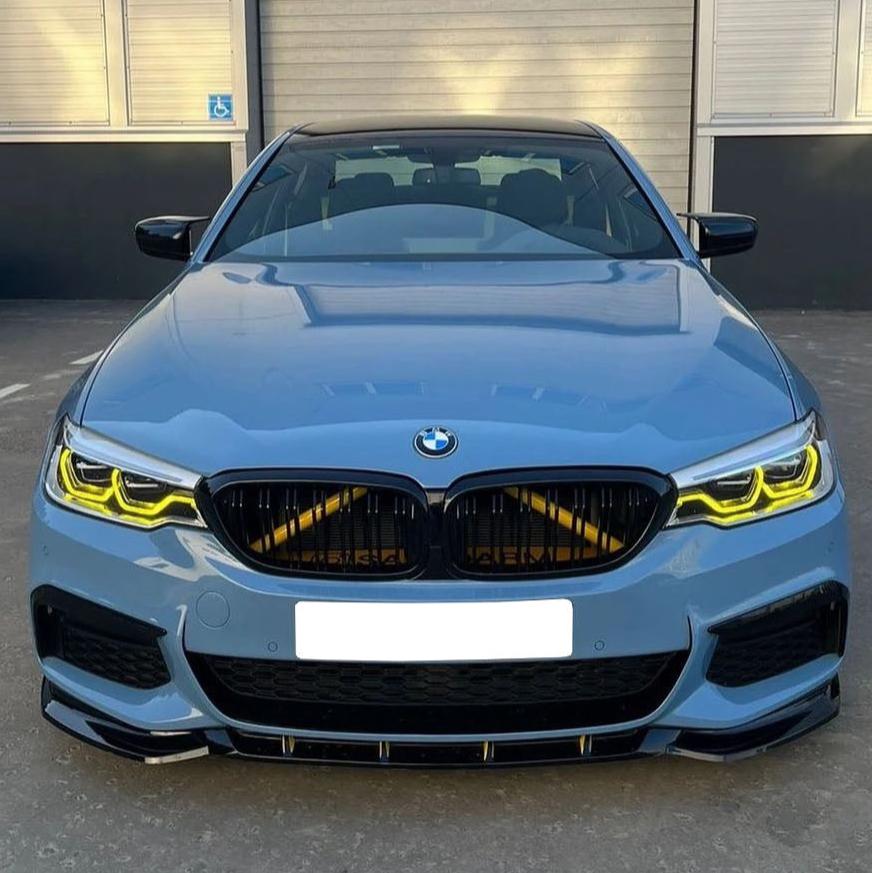 A blue BMW parked in front of a building, displaying its front grille and yellow-highlighted headlights. The building has gray metal shutters and a handicap parking sign.