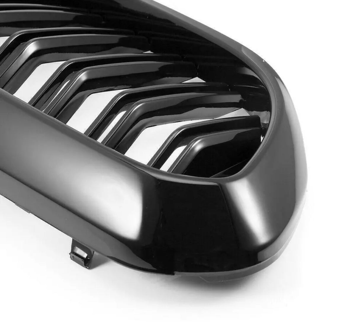 A glossy black car grille features parallel slats, resting against a plain white background.