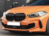 A bright orange BMW car is parked, displaying a prominent front grille and sleek headlights on a street with a building entrance nearby. The license plate is white.