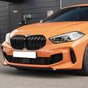 A bright orange BMW car is parked, displaying a prominent front grille and sleek headlights on a street with a building entrance nearby. The license plate is white.