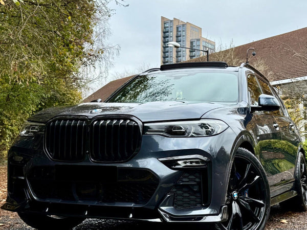 A sleek, black SUV is parked on a wet, leaf-covered road, surrounded by trees and buildings in the background, under a cloudy sky.