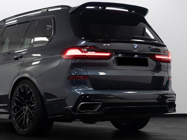 An SUV, stationary, is shown from the rear with illuminated taillights. The model is labeled "BMW X7 M50d." Its dark color contrasts against a bright, indoor background.