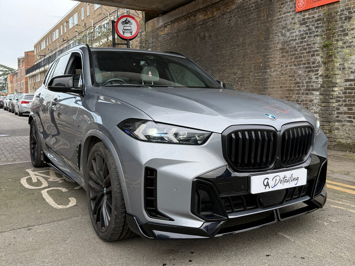 A silver SUV is parked under a low bridge beside a brick wall, displaying two signs with text: "524 to 514" and "G Detailing" on the license plate.