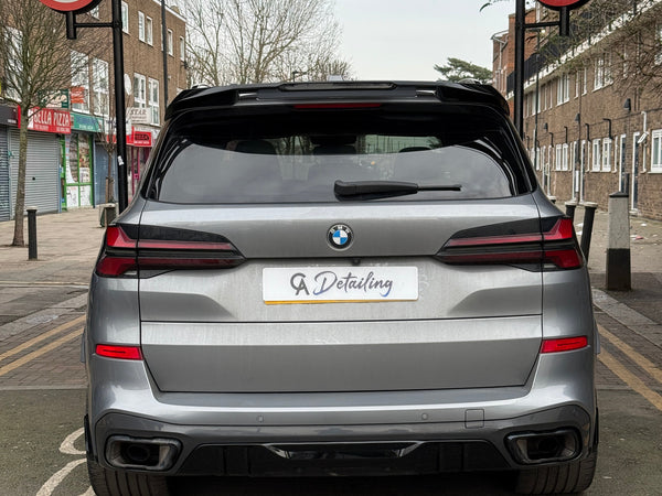 A silver car with a "GA Detailing" plate is parked on a street with no-entry signs for cars and motorcycles. Nearby, shops and residential buildings line the road.