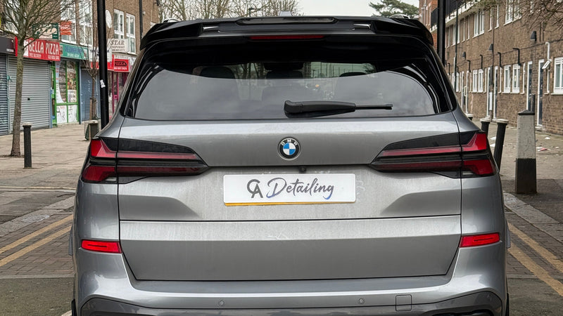 A silver car with a "GA Detailing" plate is parked on a street with no-entry signs for cars and motorcycles. Nearby, shops and residential buildings line the road.