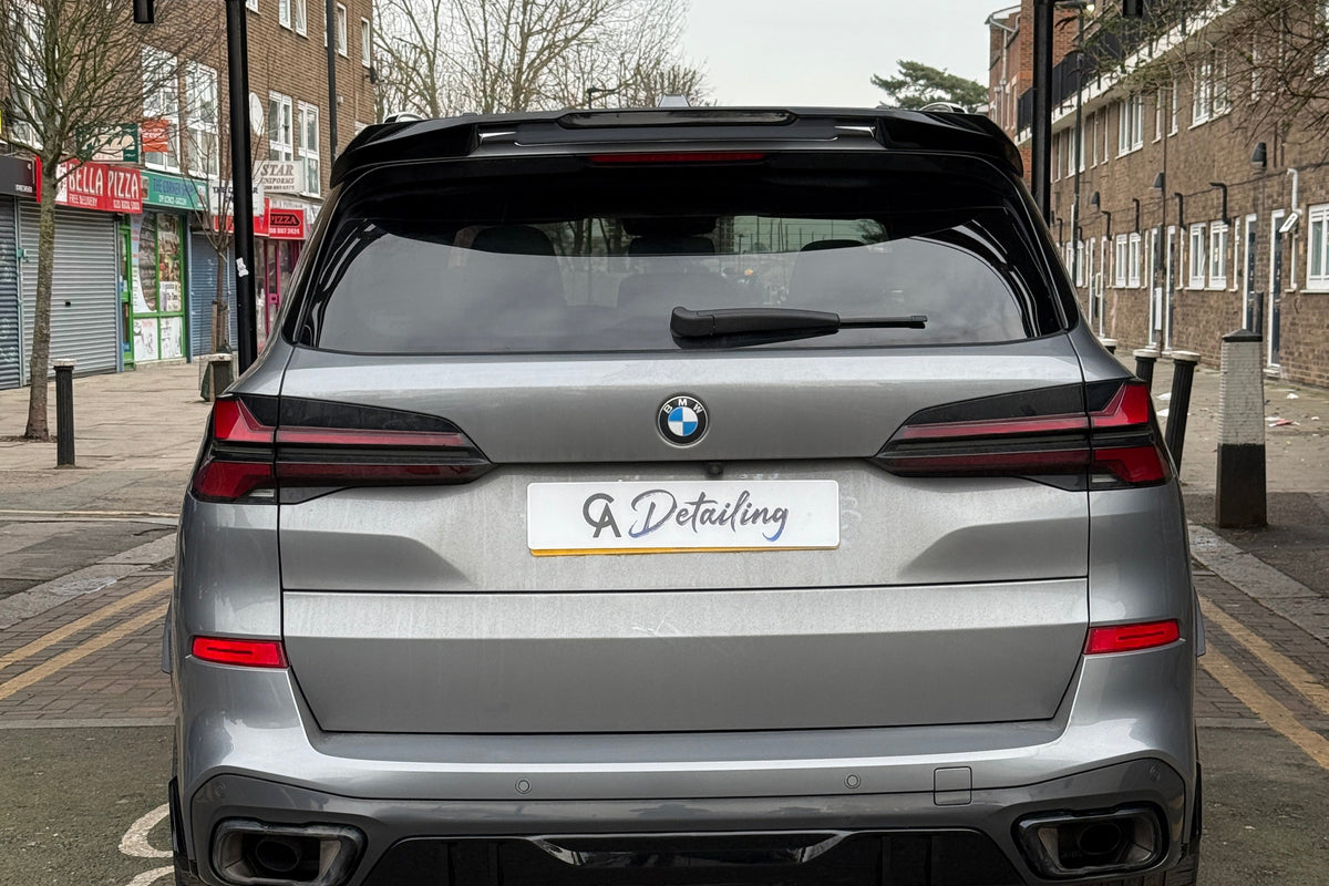 A silver car with a "GA Detailing" plate is parked on a street with no-entry signs for cars and motorcycles. Nearby, shops and residential buildings line the road.