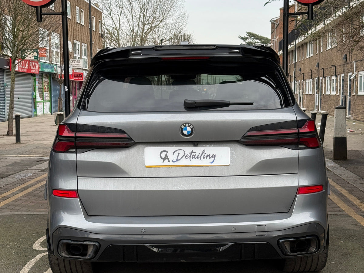 A silver car with a "GA Detailing" plate is parked on a street with no-entry signs for cars and motorcycles. Nearby, shops and residential buildings line the road.