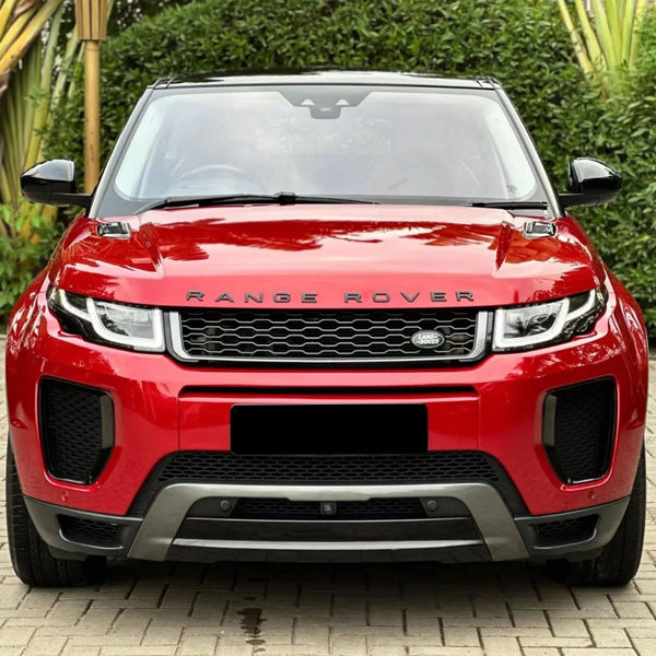 A red Range Rover is parked on a brick driveway, surrounded by lush greenery. The front of the car prominently displays the "RANGE ROVER" and "LAND ROVER" logos.