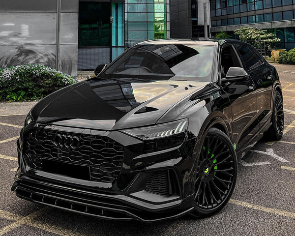 A sleek black car is parked on a lot, featuring green-accented wheels, in front of a modern glass and concrete building.