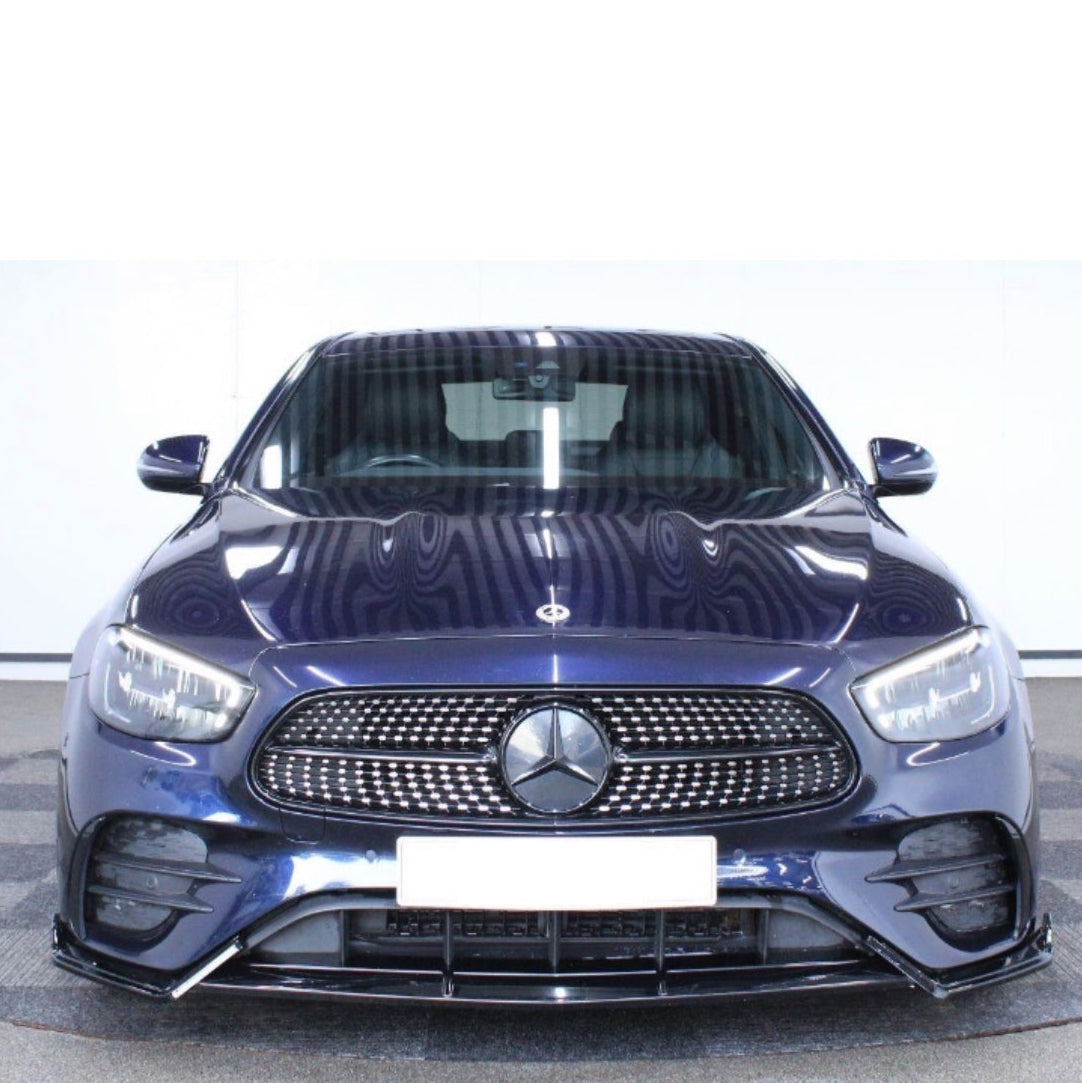 A dark blue Mercedes car is parked indoors, facing forward, highlighting its grille and emblem with a bright, reflective surface. The background is a neutral indoor setting.