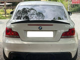 A white BMW car is parked, reflecting tree silhouettes on its rear window. It is situated on a gravel path near a 