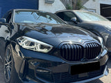 A sleek black BMW parked on a sunny day, next to another car, in front of a brick building with a blue garage door. Signs read 