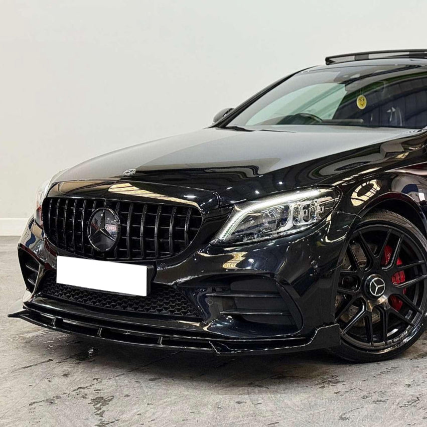 A black car with a sleek front grille and headlights is parked indoors on a concrete floor. The vehicle features black alloy wheels and red brake calipers. The license plate is blank.