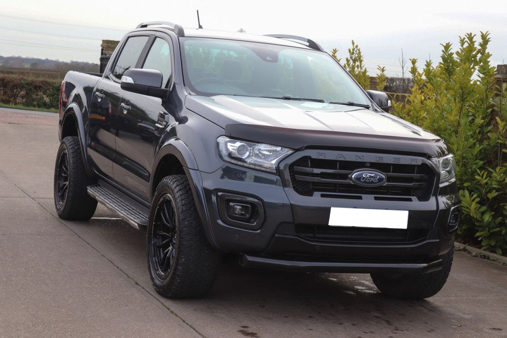 A dark gray Ford Ranger pickup truck is parked on a concrete driveway, surrounded by green foliage and a clear sky.