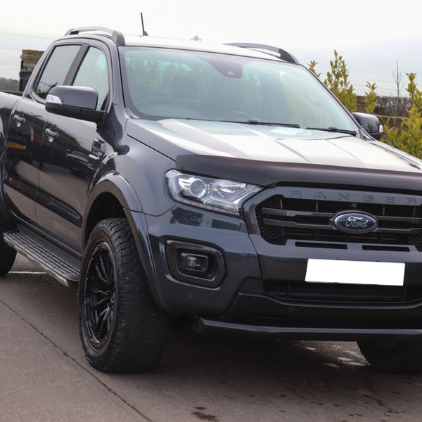 A dark gray Ford Ranger pickup truck is parked on a concrete driveway, surrounded by green foliage and a clear sky.