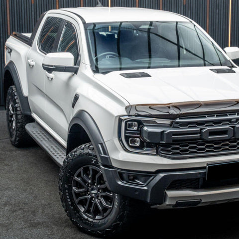 White pickup truck parked inside a building, displaying a bold grille and rugged tires. The backdrop features dark vertical panels, creating a contrasting modern industrial atmosphere.