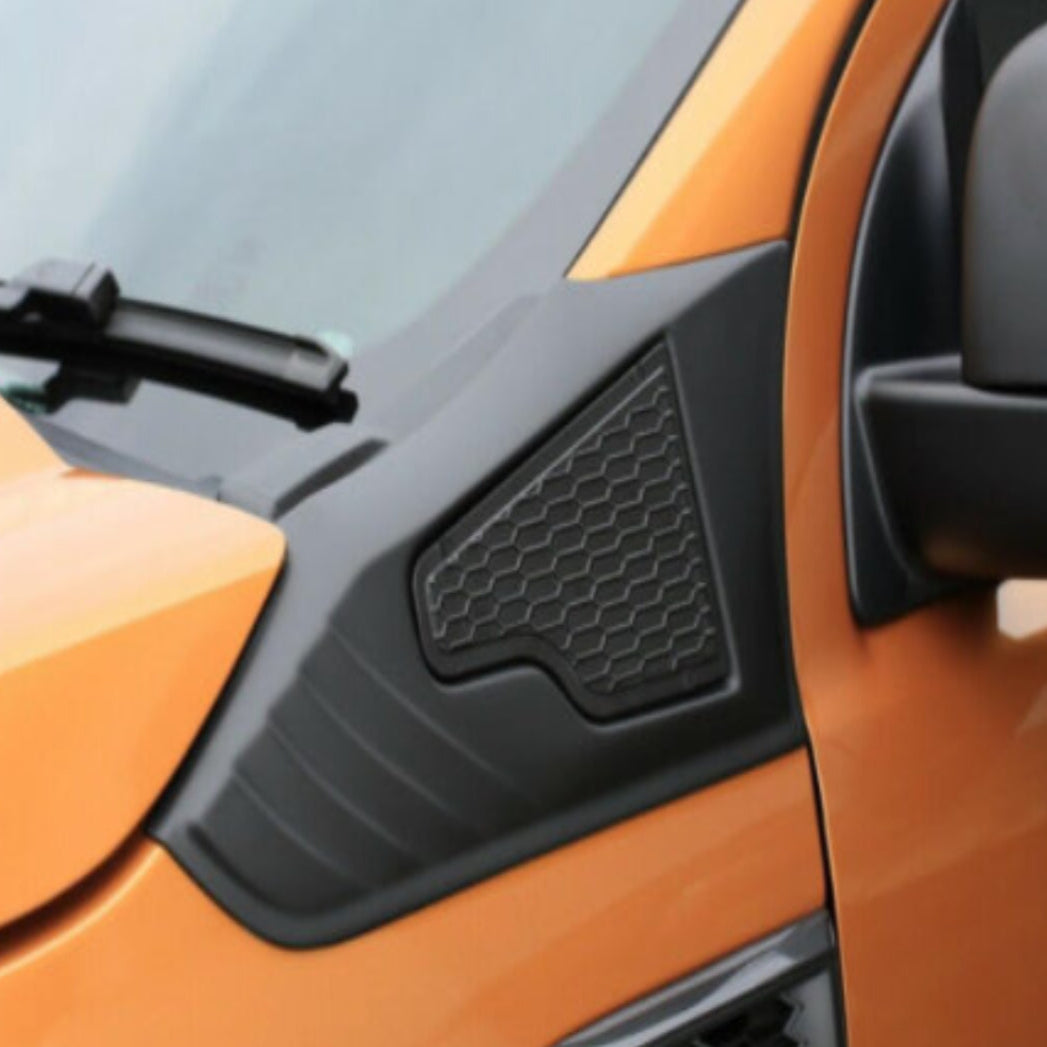 An orange vehicle with a black plastic panel featuring a hexagonal pattern, located near the side mirror and windshield wiper, set against a smooth, light background.