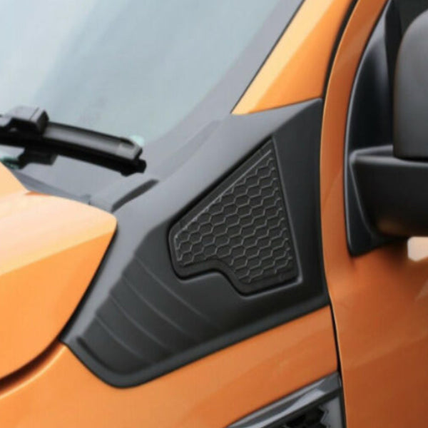 An orange vehicle with a black plastic panel featuring a hexagonal pattern, located near the side mirror and windshield wiper, set against a smooth, light background.