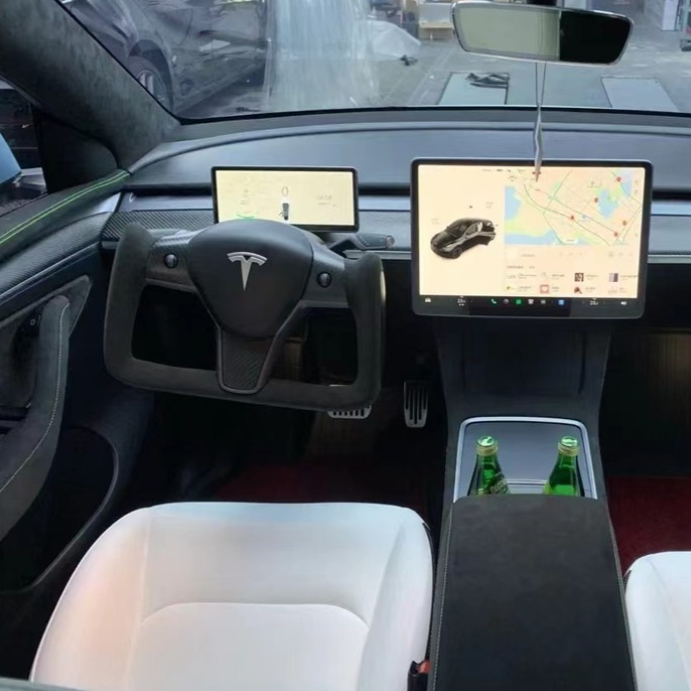 Yoke-style steering wheel with a central Tesla logo; two screens display maps and vehicle data; white seats and two green bottles in the center console; modern car interior.