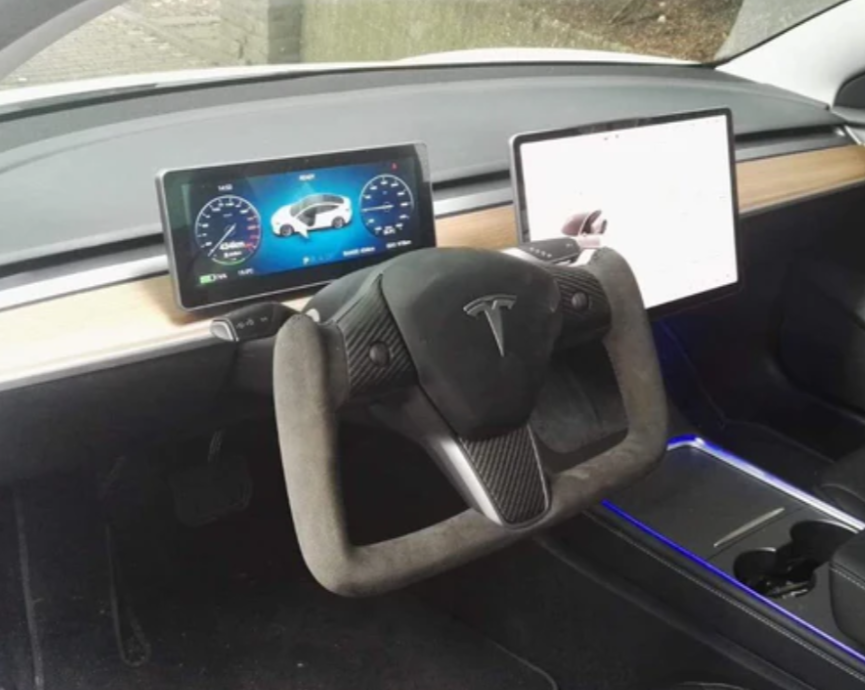 A Tesla yoke steering wheel surrounded by two digital displays in a minimalist car dashboard, featuring wood panel accents and ambient blue lighting from the center console.