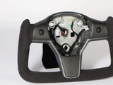 A square-shaped racing steering wheel sits against a white background. It is made of carbon fiber and suede, with visible internal components and wiring in the center area.