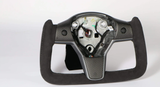 A square-shaped racing steering wheel sits against a white background. It is made of carbon fiber and suede, with visible internal components and wiring in the center area.