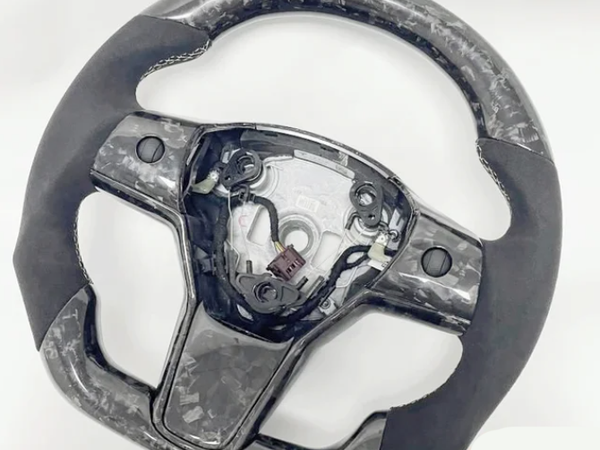 A steering wheel with a marbled pattern and missing central cover, exposing internal wiring and mechanisms, set against a plain white background.