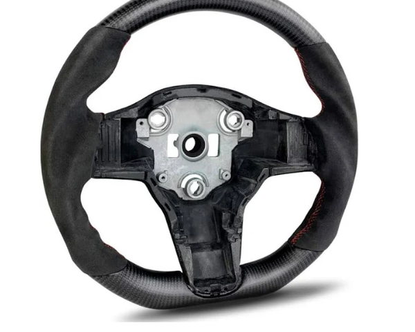 A carbon fiber steering wheel with a central metal hub is positioned upright. It features red stitching and lacks controls, set against a plain white background.