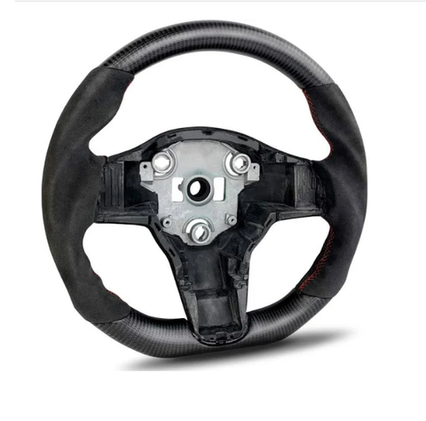 A carbon fiber steering wheel with a central metal hub is positioned upright. It features red stitching and lacks controls, set against a plain white background.