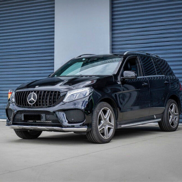 A black SUV is parked on a concrete surface in front of a building with blue, corrugated metal doors. The Mercedes-Benz emblem is prominently displayed on the grille.